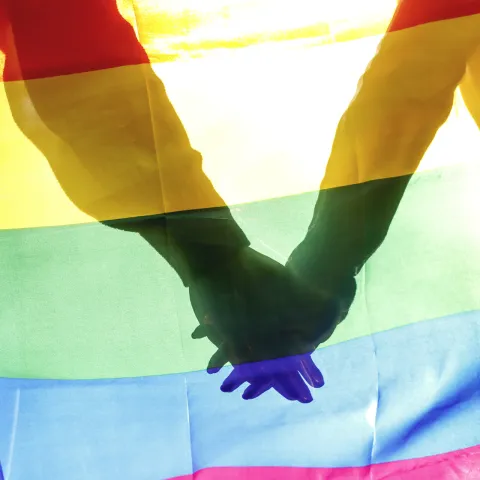 People, homosexuality, same-sex marriage, gay and love concept - close up of happy male gay couple hugging and holding rainbow flag